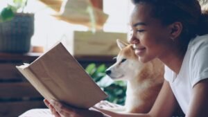 Dog owner reading a book beside her dog at home
